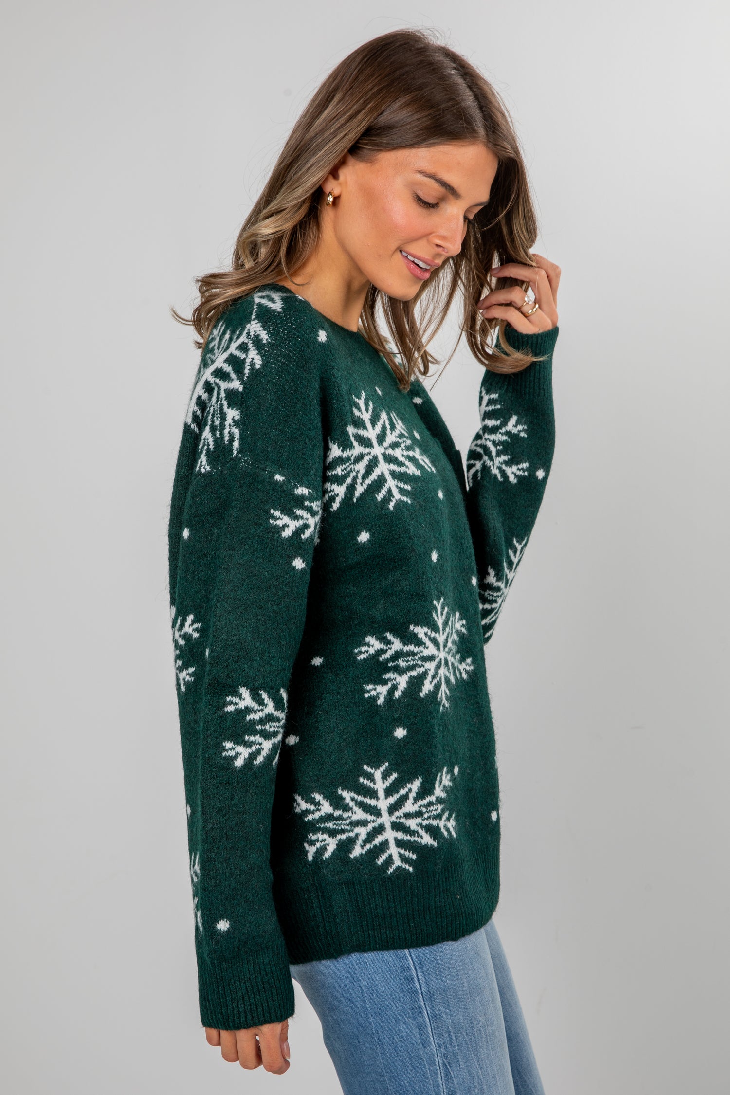 Woman wearing a green sweater with snowflake patterns on a plain background