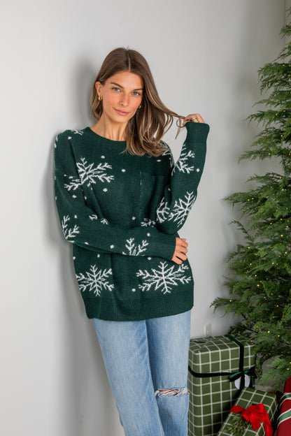 Woman wearing a green sweater with snowflake patterns in front of a Christmas tree and presents.