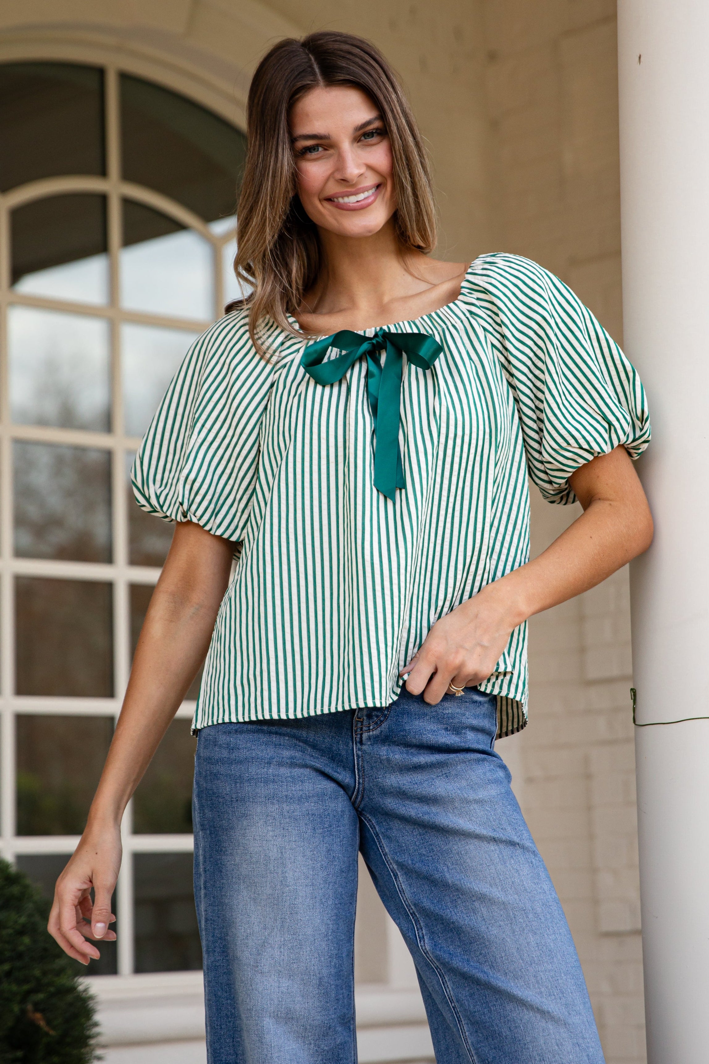 Woman wearing a green and white striped blouse with a bow tie, standing outdoors.