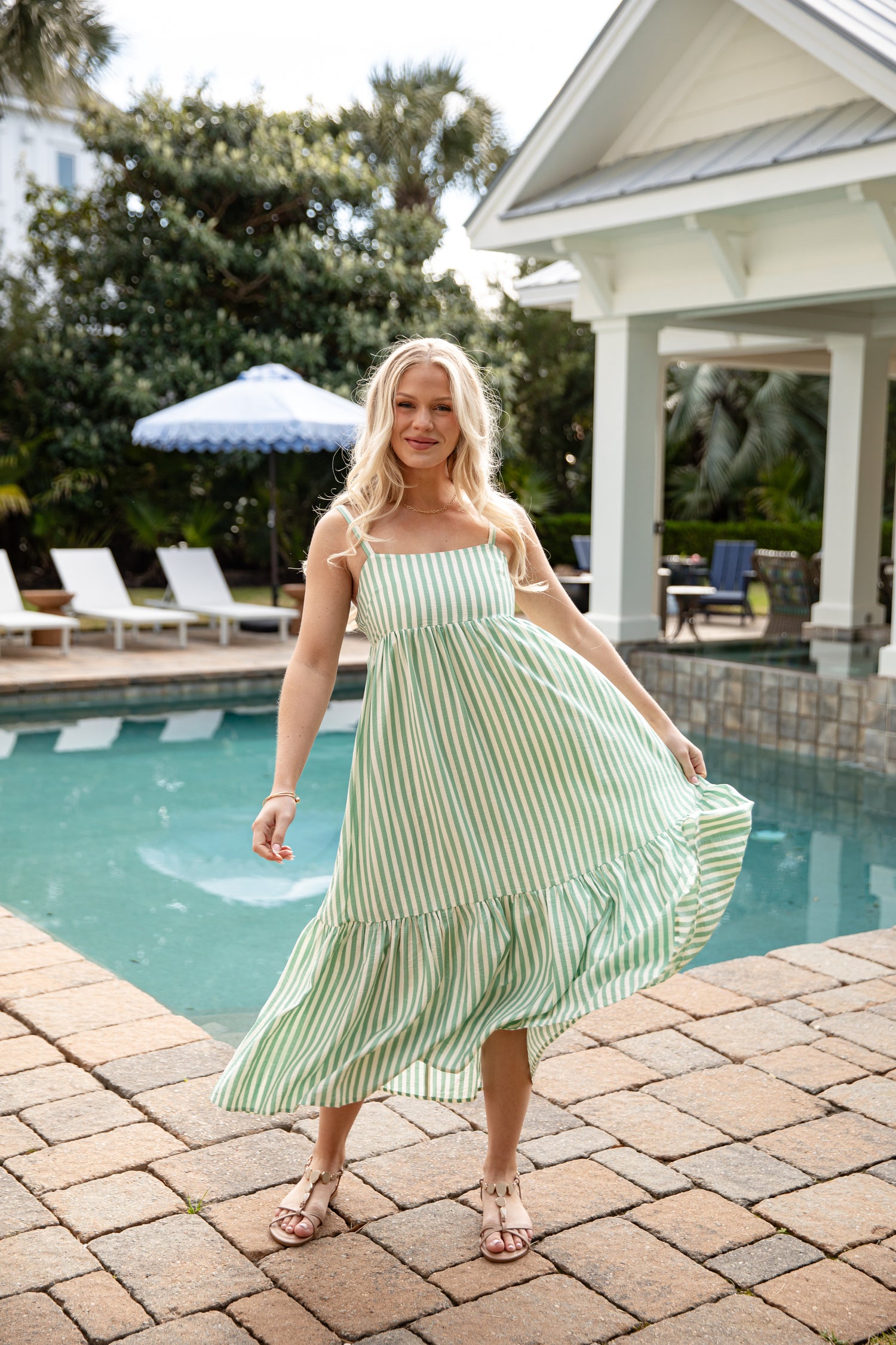 Woman in a green and white striped dress standing by a poolside.