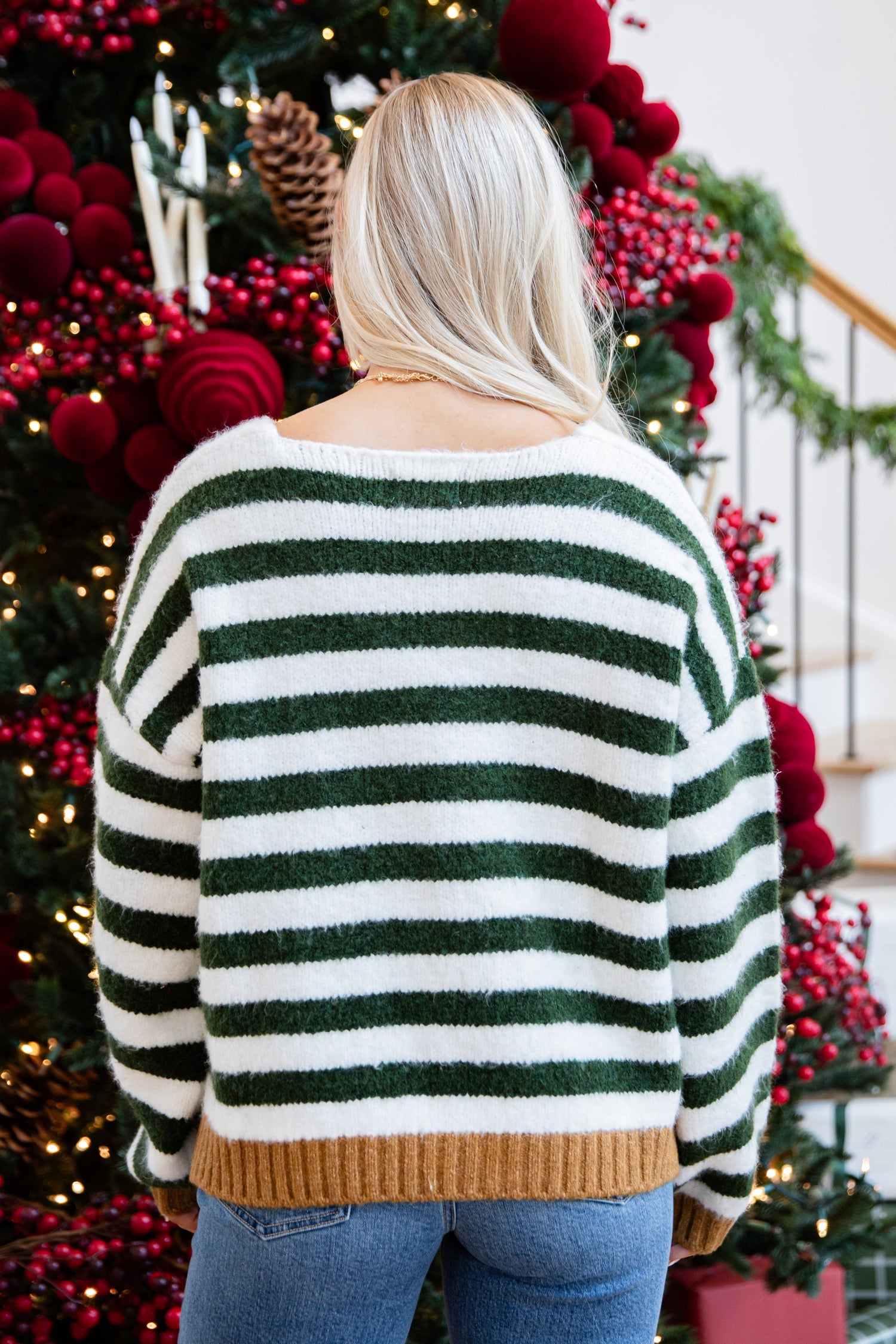 Person wearing a green and white striped sweater in front of a decorated Christmas tree.
