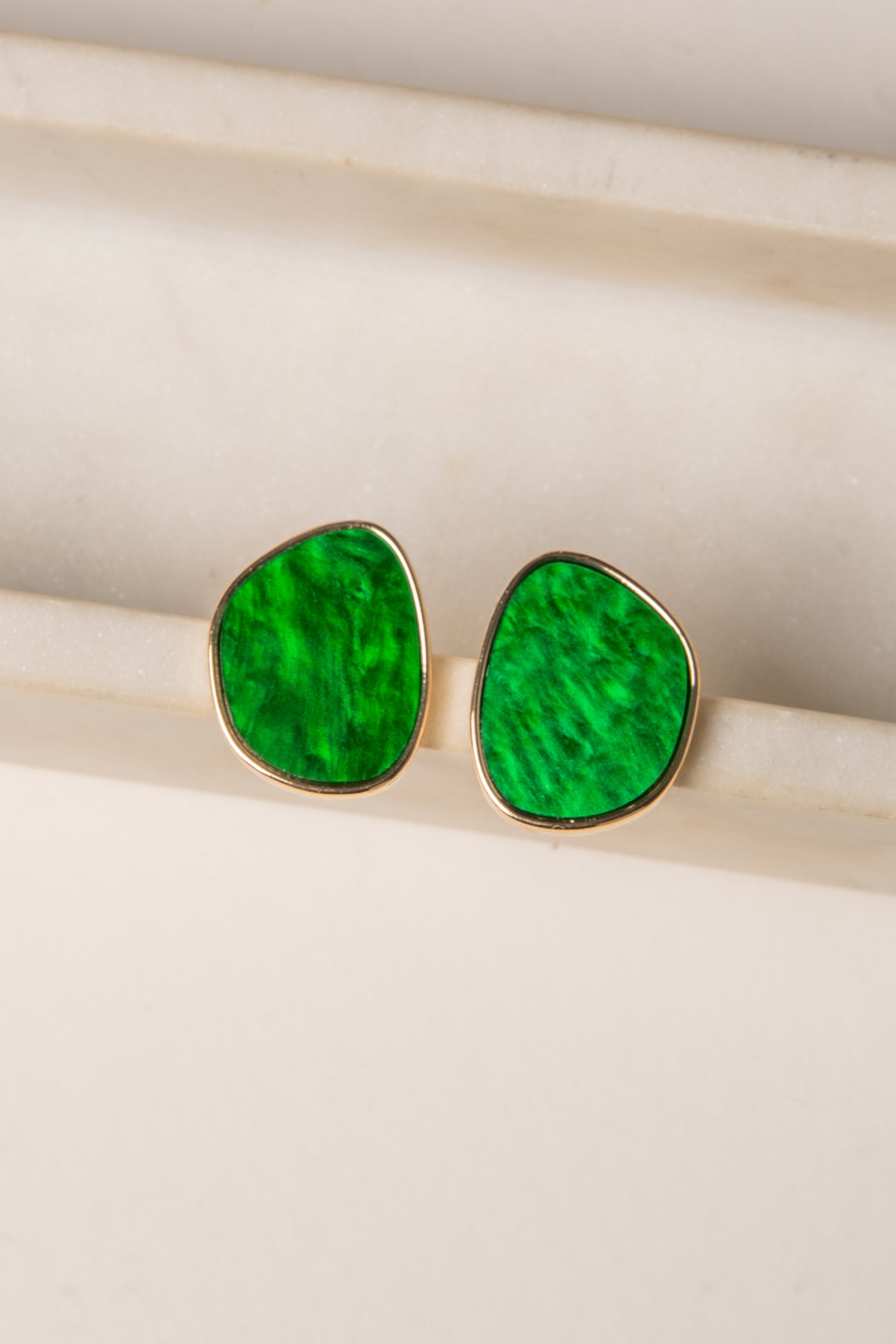 Green teardrop earrings with gold rims on a light wooden surface