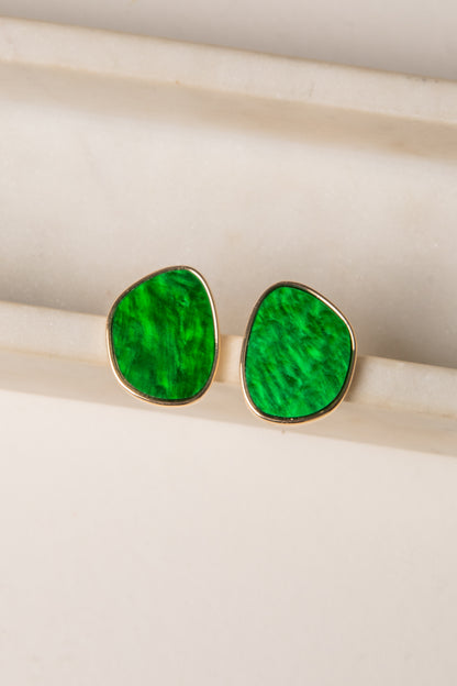 Green teardrop earrings with gold rims on a light wooden surface