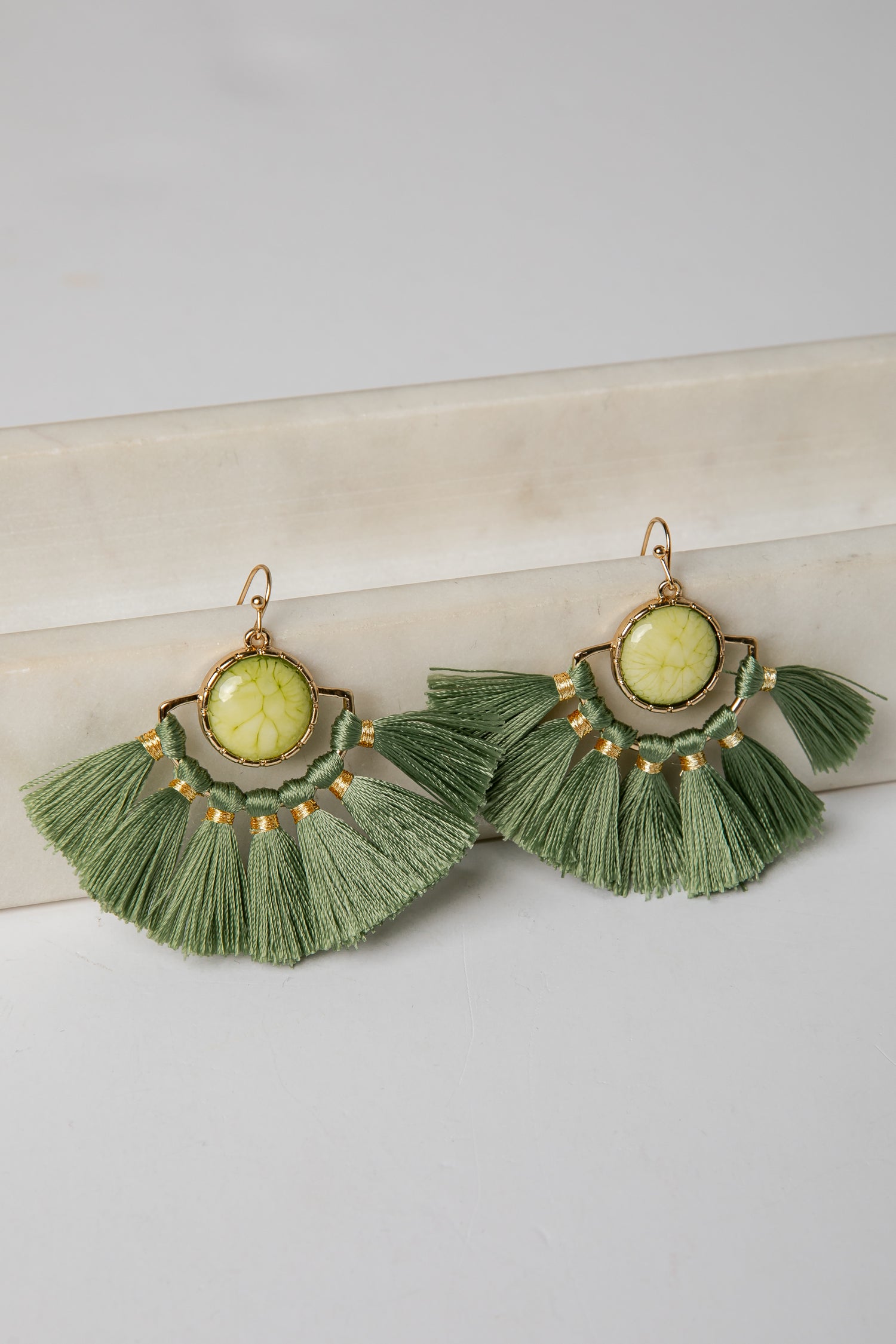 Green tassel earrings with gold accents on a light surface