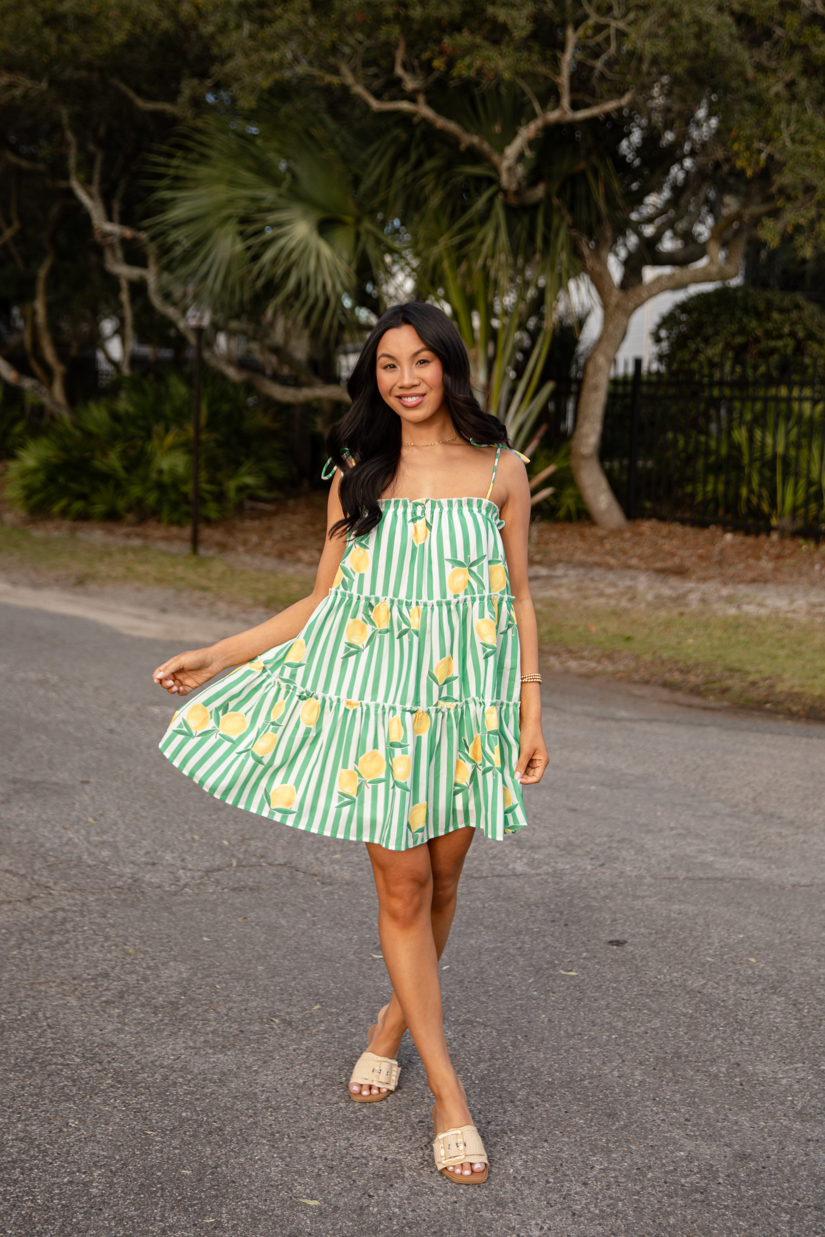 Woman in a green and white striped dress with lemon pattern walking on a road.