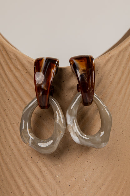 Pair of earrings with tortoiseshell and clear design on a beige surface