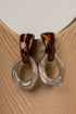 Pair of earrings with tortoiseshell and clear design on a beige surface