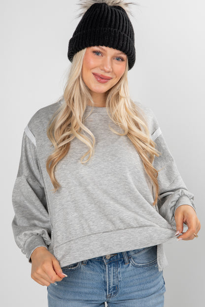 Woman wearing a gray sweatshirt, black beanie, and blue jeans on a white background