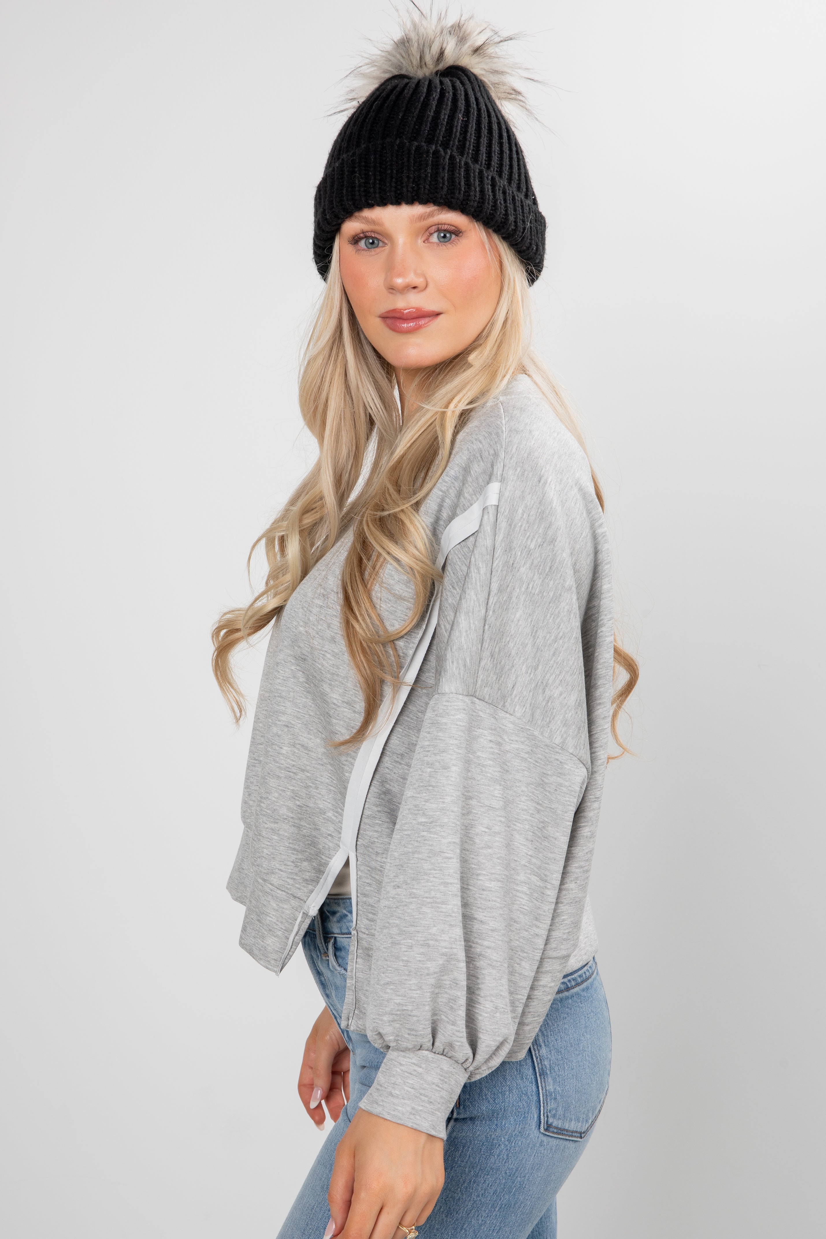 Woman wearing a gray cardigan, black knit beanie, and blue jeans on a white background