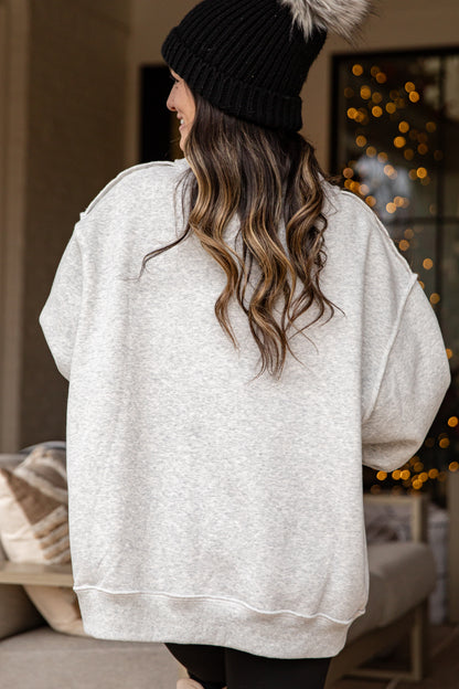 Person wearing a white oversized sweater and black beanie in a cozy indoor setting with blurred lights.