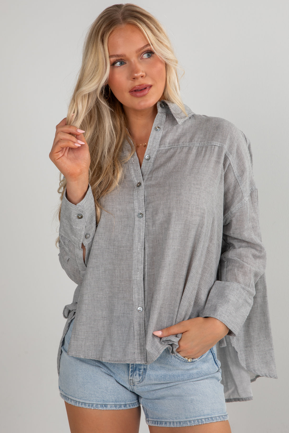 Woman wearing a gray button-up shirt and denim shorts on a plain background