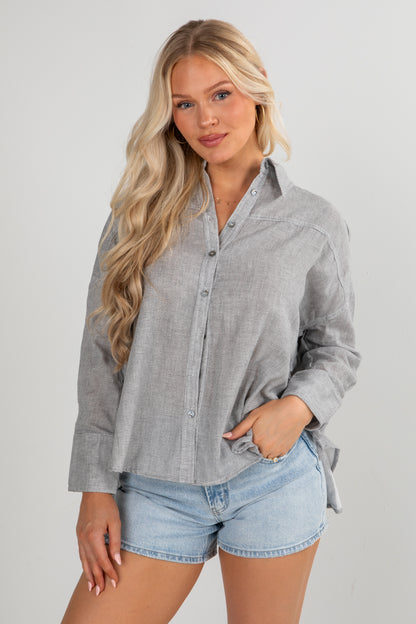 Woman wearing a gray button-up shirt and denim shorts on a plain background