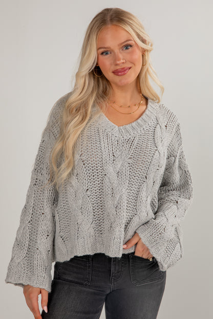 Woman wearing a gray cable knit sweater against a plain background