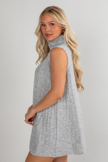 Woman wearing a sleeveless gray dress against a plain background