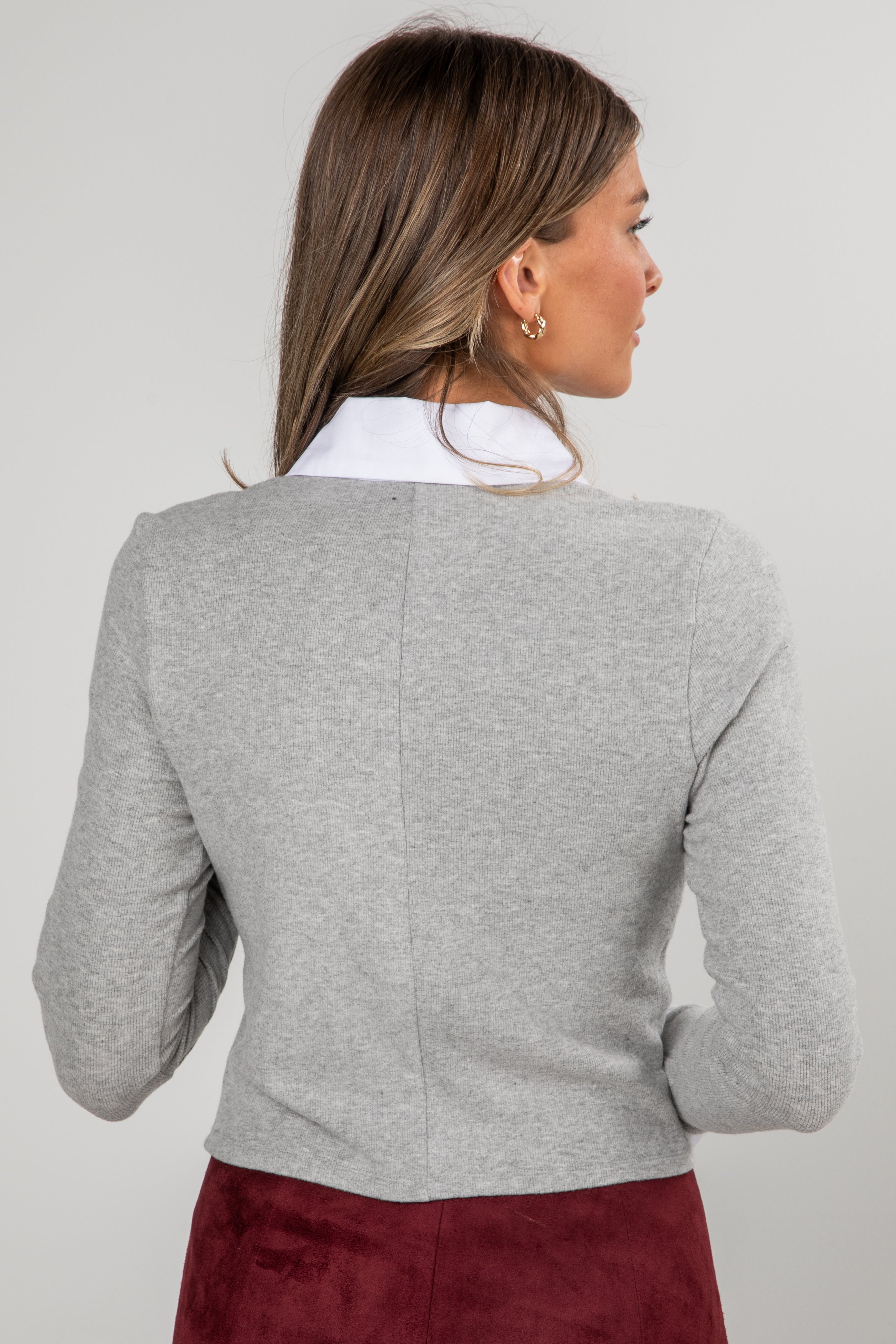 Woman wearing a gray blazer over a white shirt with a plain background