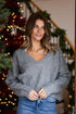 Woman wearing a gray sweater and blue jeans standing in front of a decorated Christmas tree.