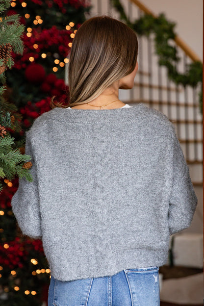 Person wearing a gray sweater in front of a decorated Christmas tree.