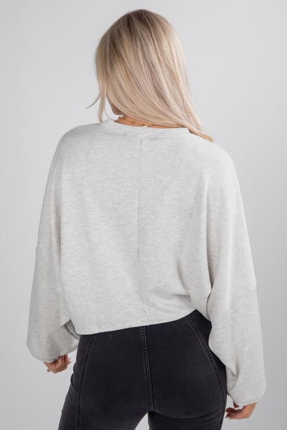 Person wearing a light gray sweater and dark pants on a plain background