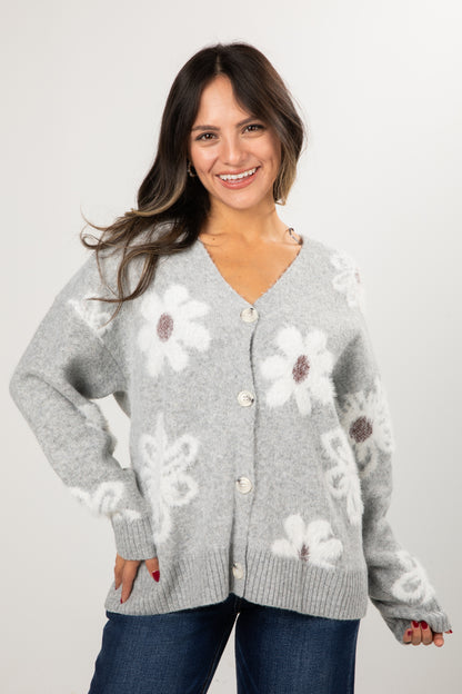 Woman wearing a gray cardigan with floral patterns on a plain background