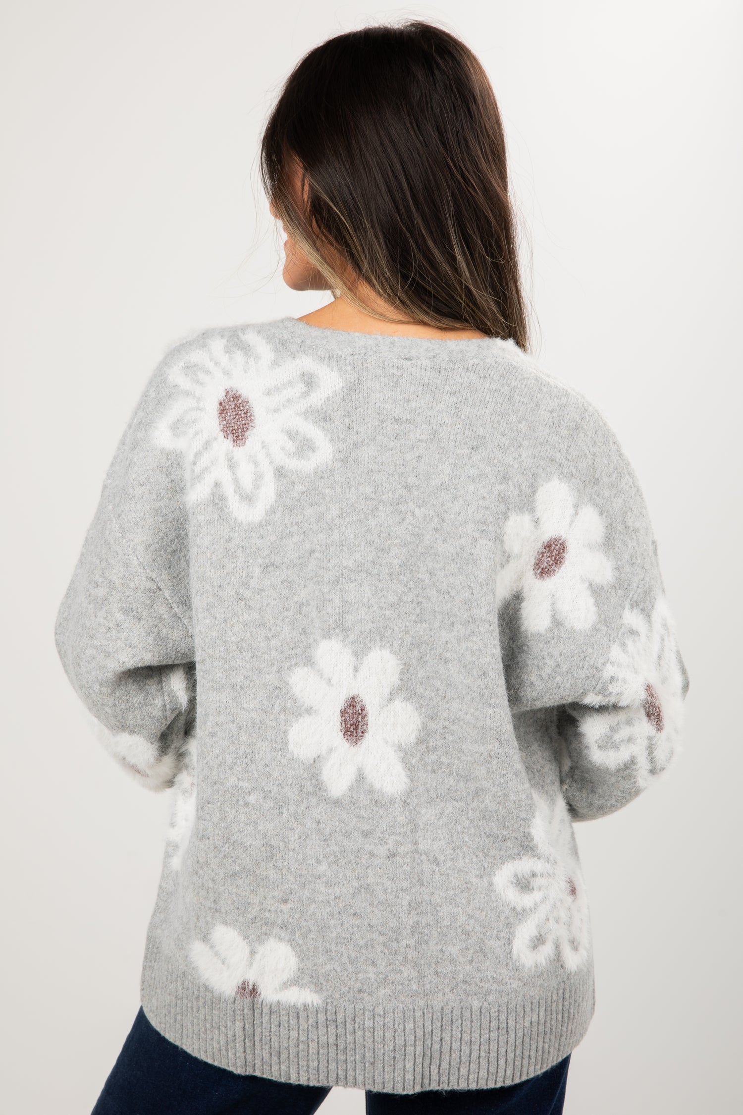 Gray sweater with white floral patterns worn by a person on a plain background