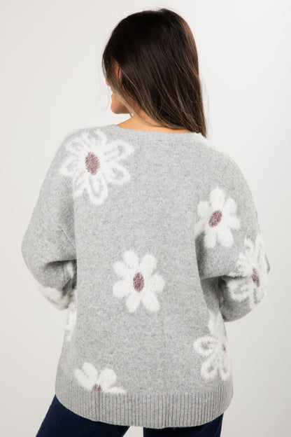 Gray sweater with white floral patterns worn by a person on a plain background