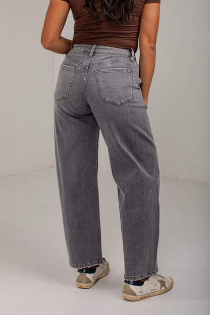 A person shown from the back wearing gray wide-leg jeans, a brown ribbed top, and distressed sneakers in a plain studio setting.