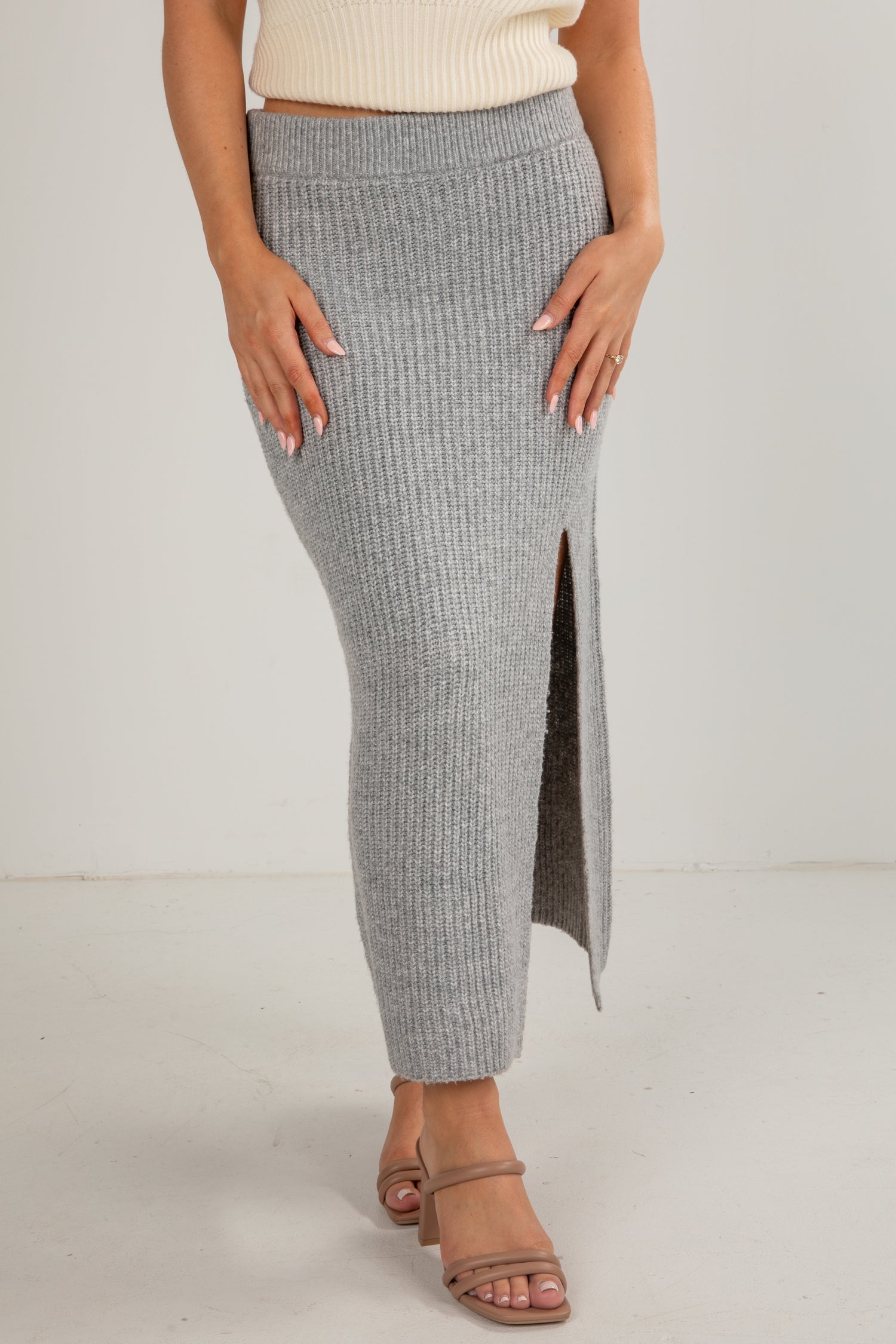 Person wearing a gray ribbed skirt with a white top on a plain background