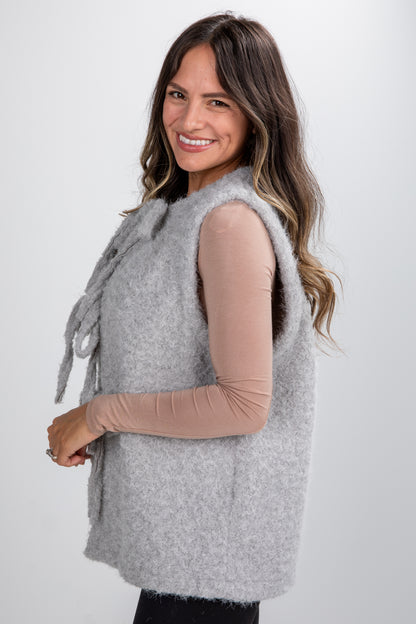 Woman wearing a gray vest over a beige long-sleeve shirt on a white background