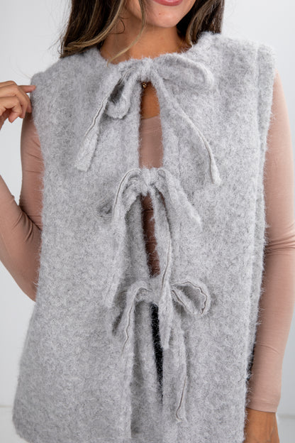 Gray fuzzy vest with tie details worn by a person on a white background