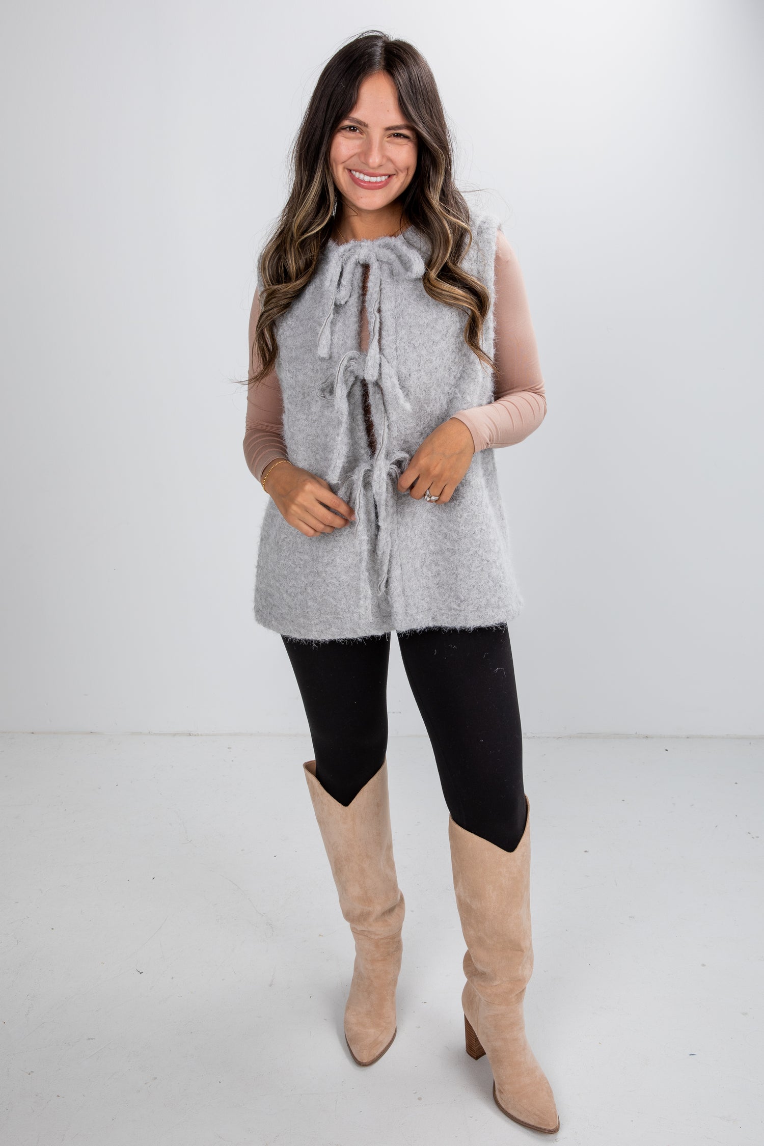 Woman wearing a gray sleeveless vest, black leggings, and beige knee-high boots on a white background
