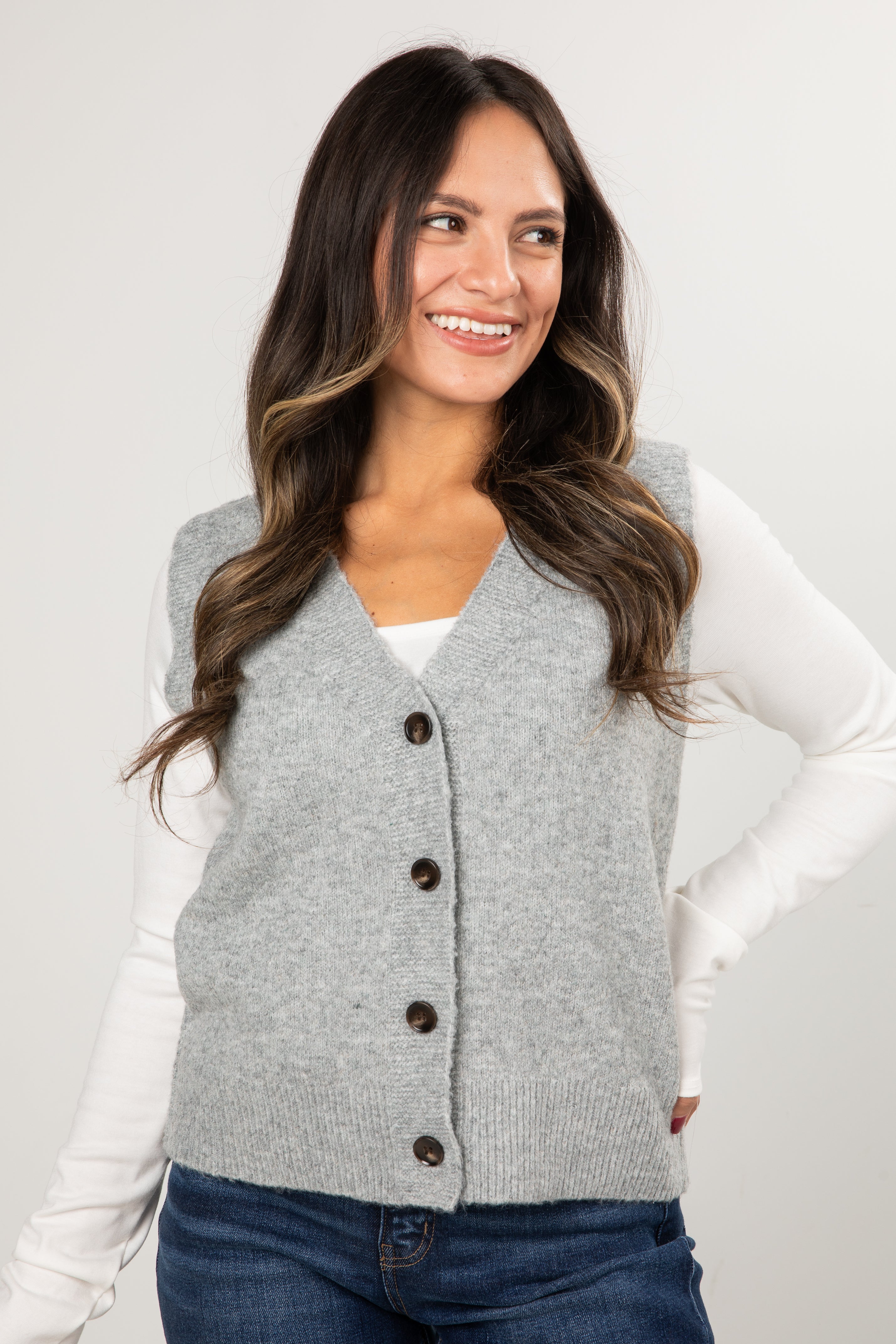 Woman wearing a gray cardigan vest with buttons on a plain background