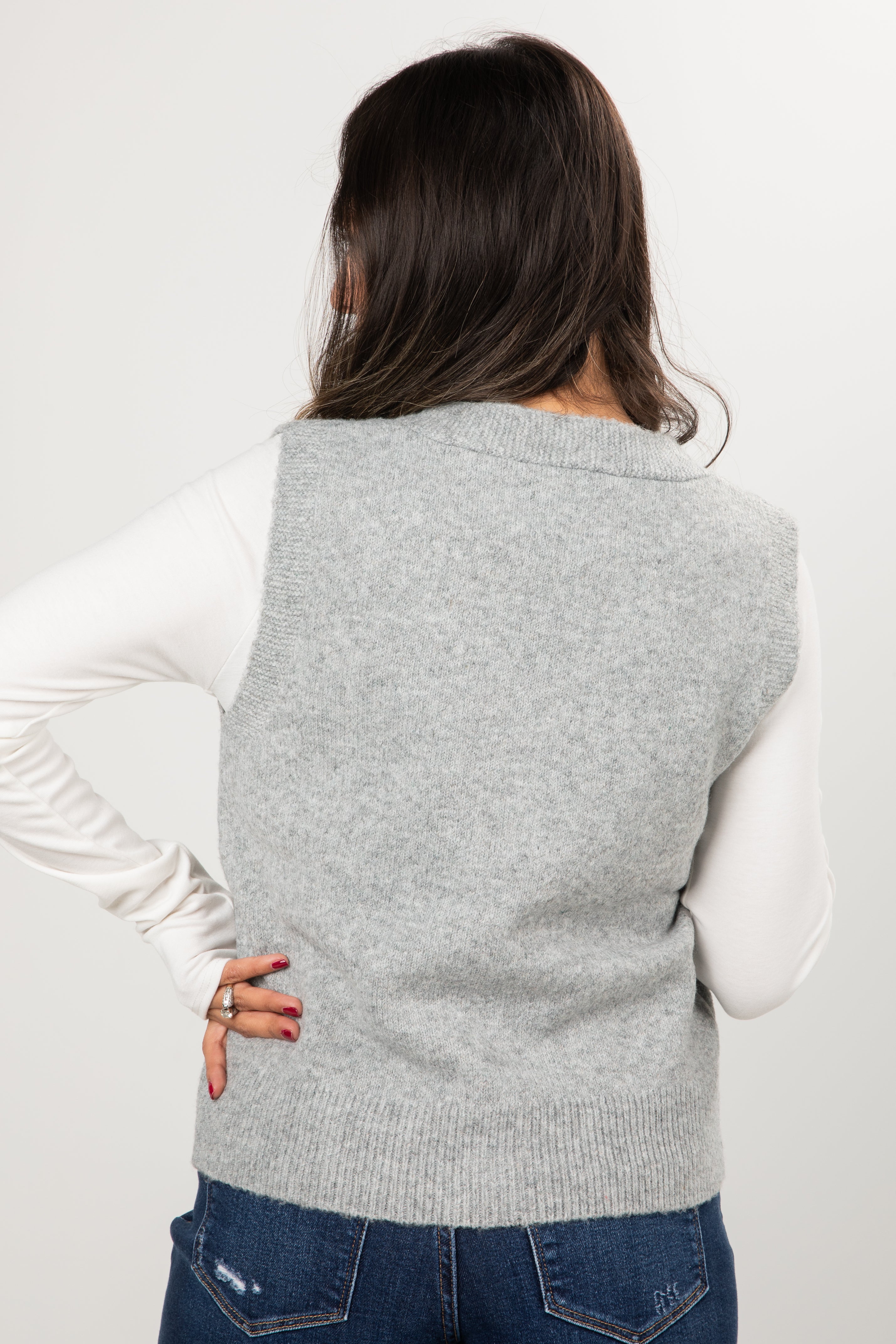 Person wearing a gray sweater vest over a white long-sleeve shirt on a plain background