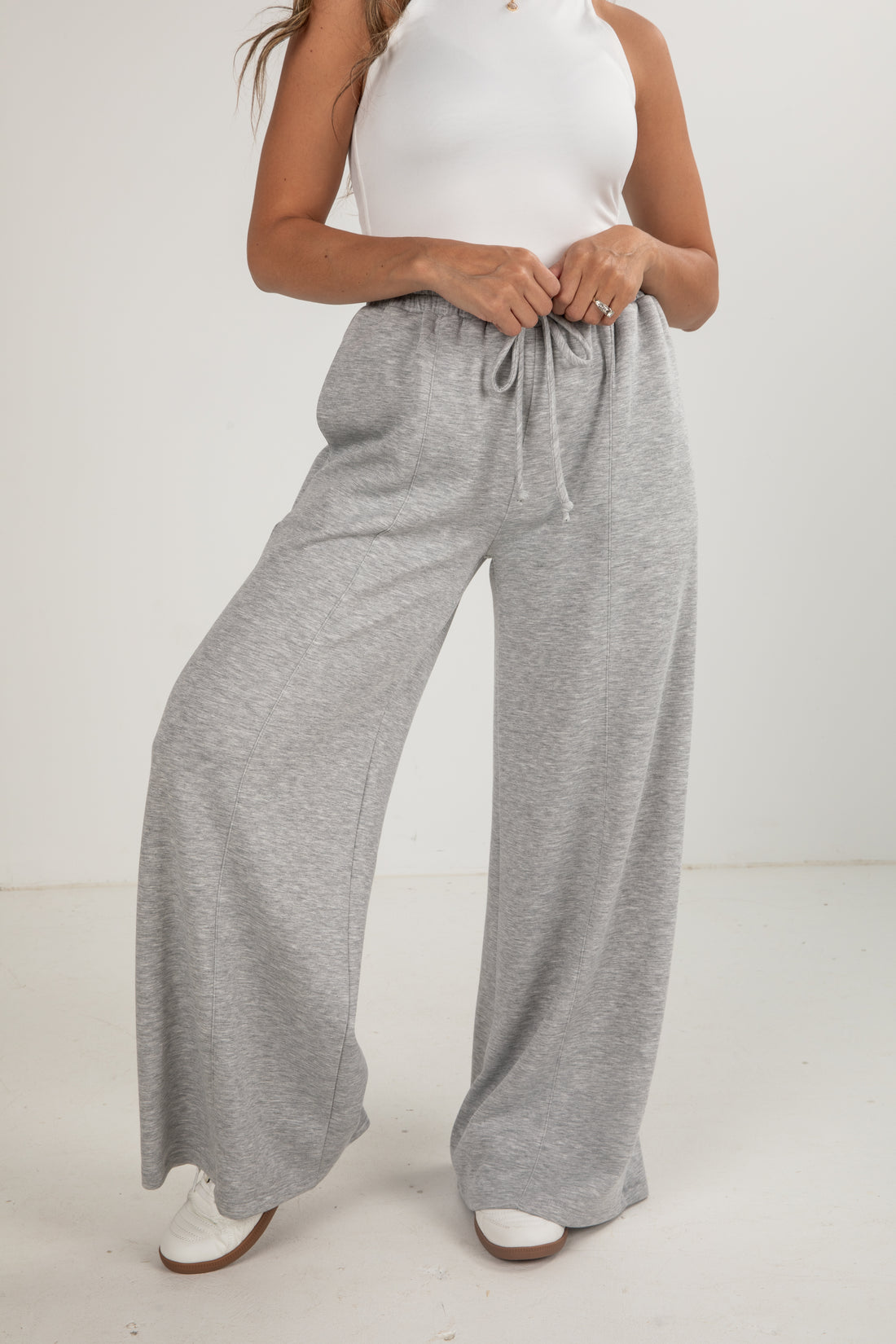 Person wearing gray wide-leg pants and a white top on a plain background