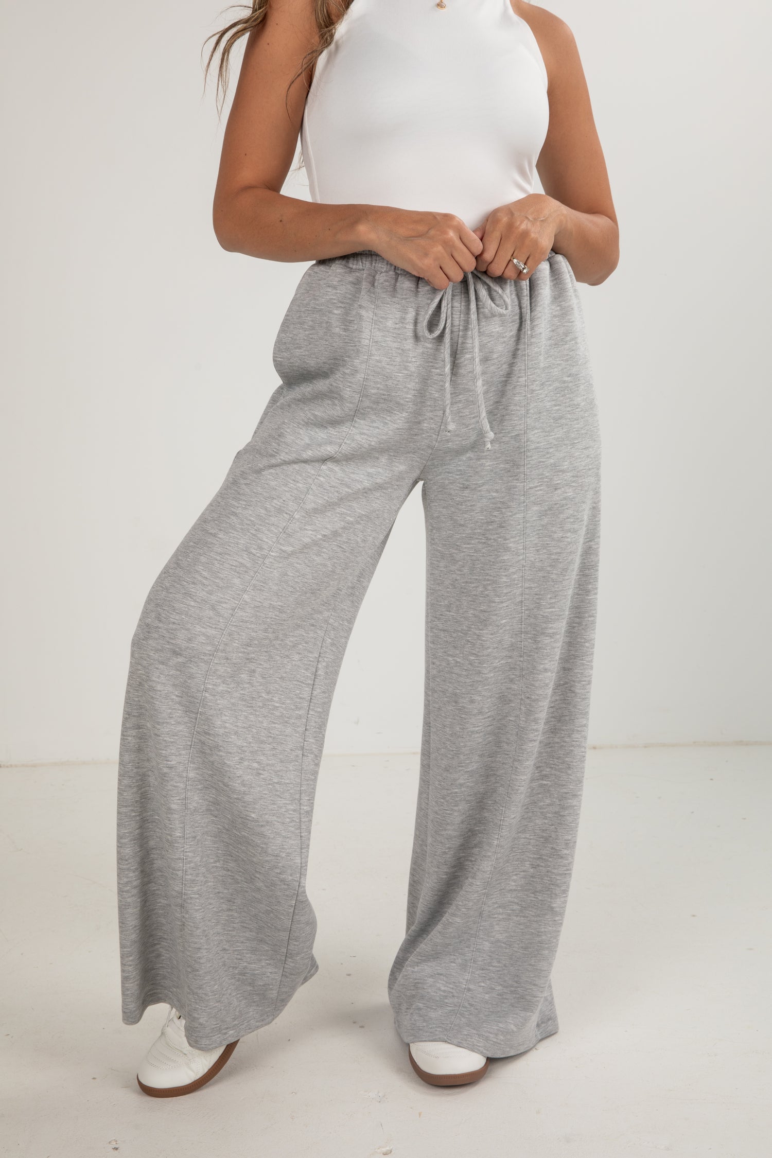 Person wearing gray wide-leg pants and a white top on a plain background