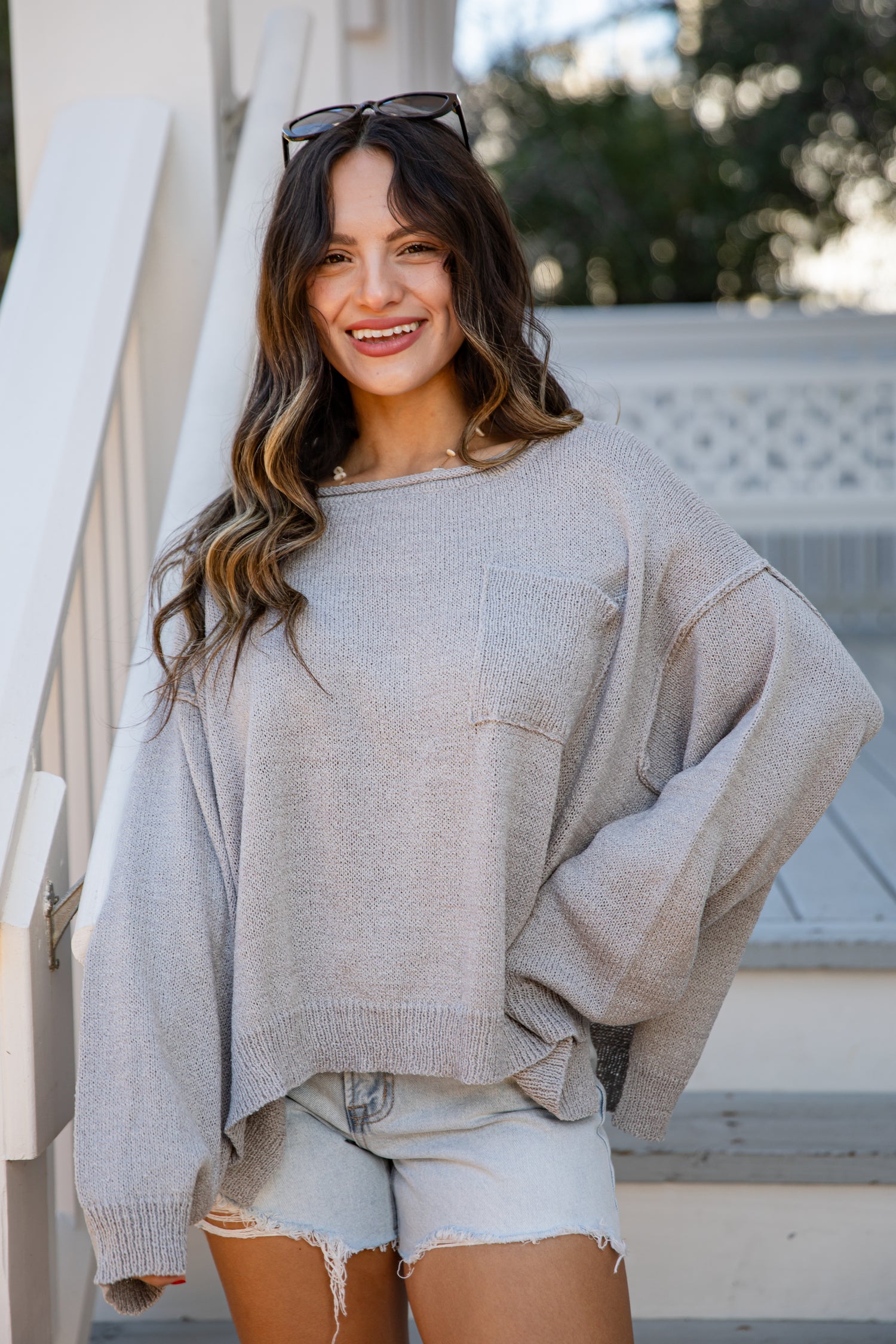 Woman wearing a light gray sweater and denim shorts standing outdoors.