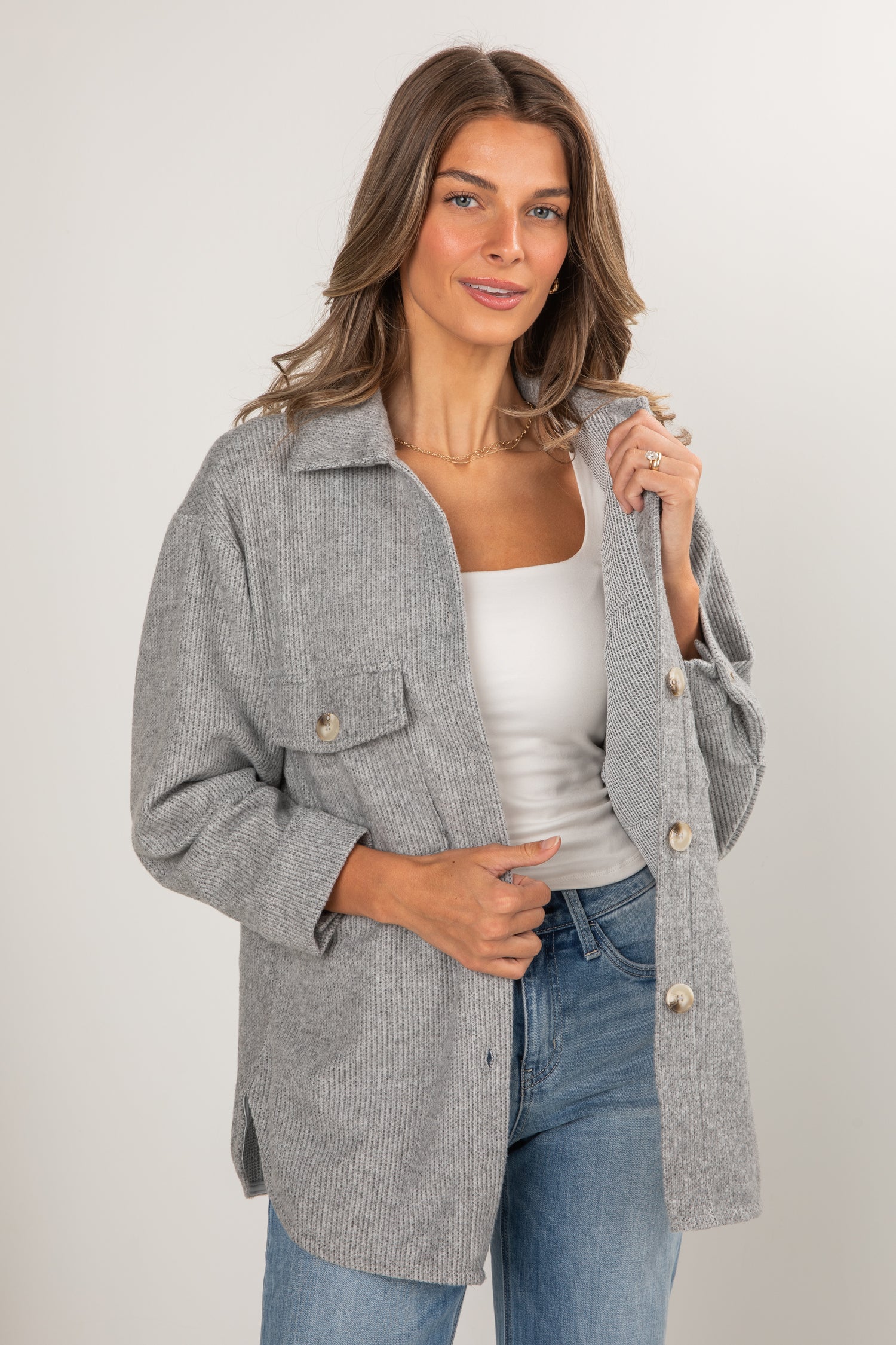 Woman wearing a gray coat over a white top and blue jeans on a plain background
