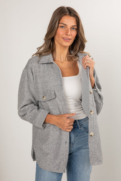 Woman wearing a gray coat over a white top and blue jeans on a plain background