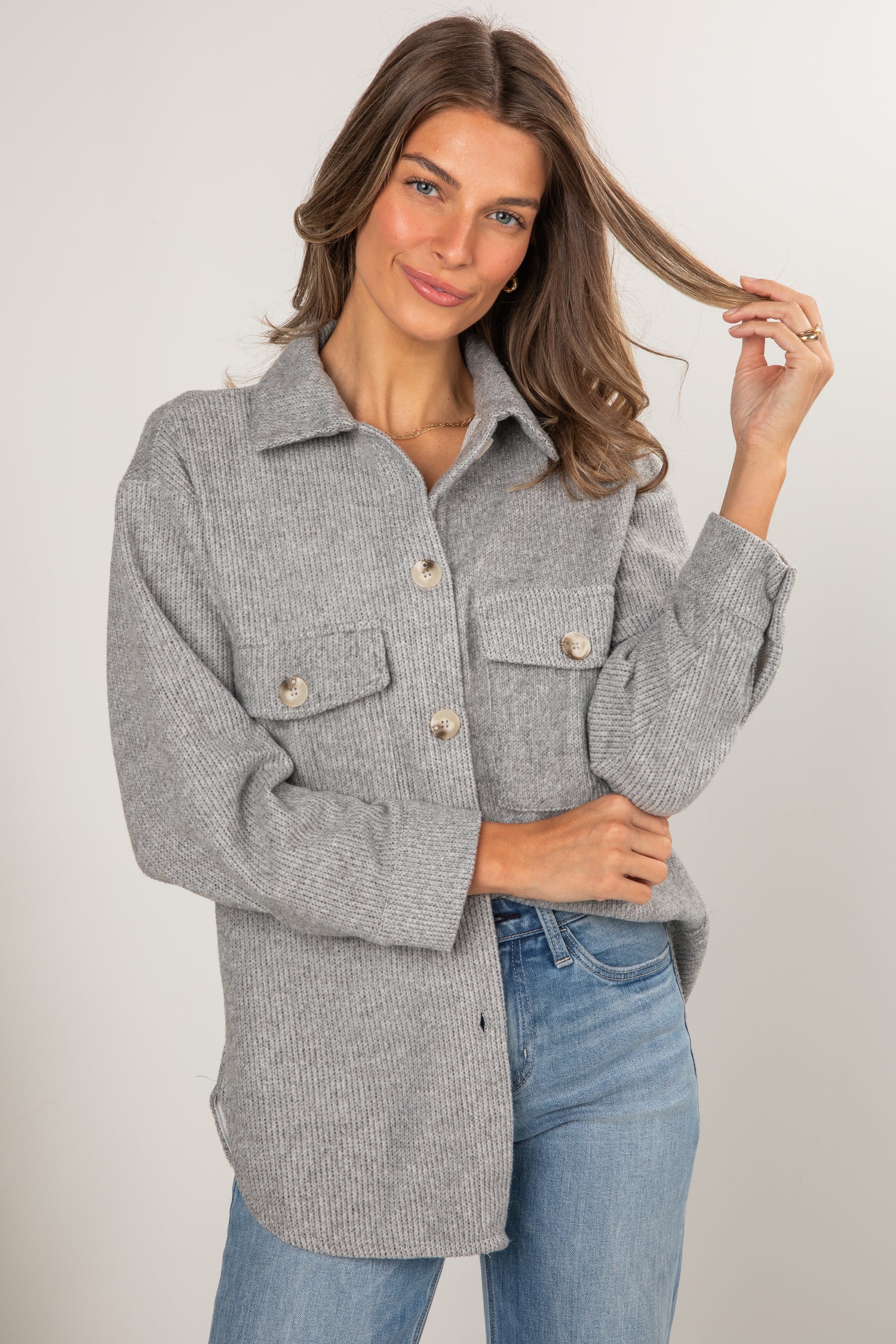 Woman wearing a gray coat and blue jeans against a plain background