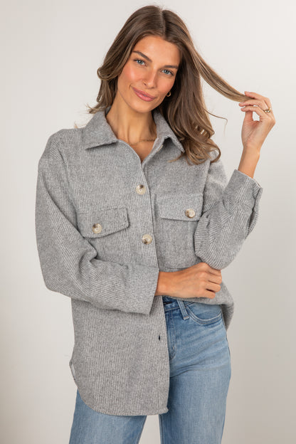 Woman wearing a gray coat and blue jeans against a plain background