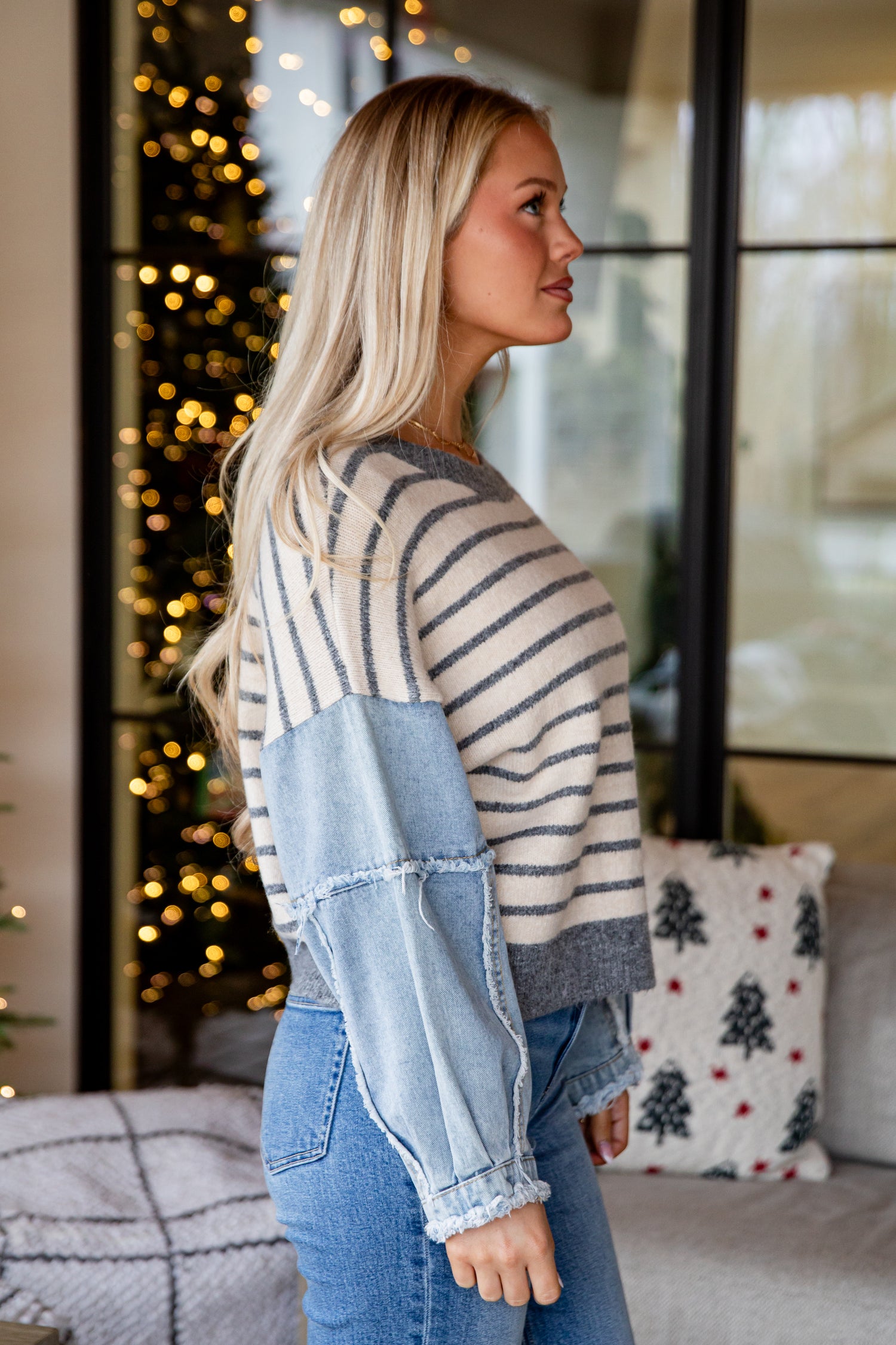 Woman wearing a striped sweater and denim jacket in a cozy living room.