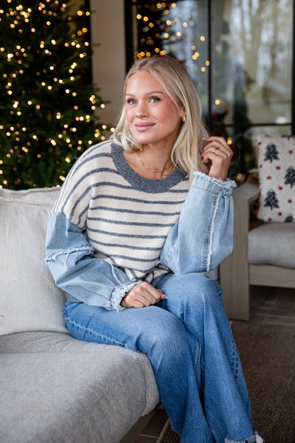Woman sitting on a couch wearing a striped sweater and denim jacket in a cozy living room.