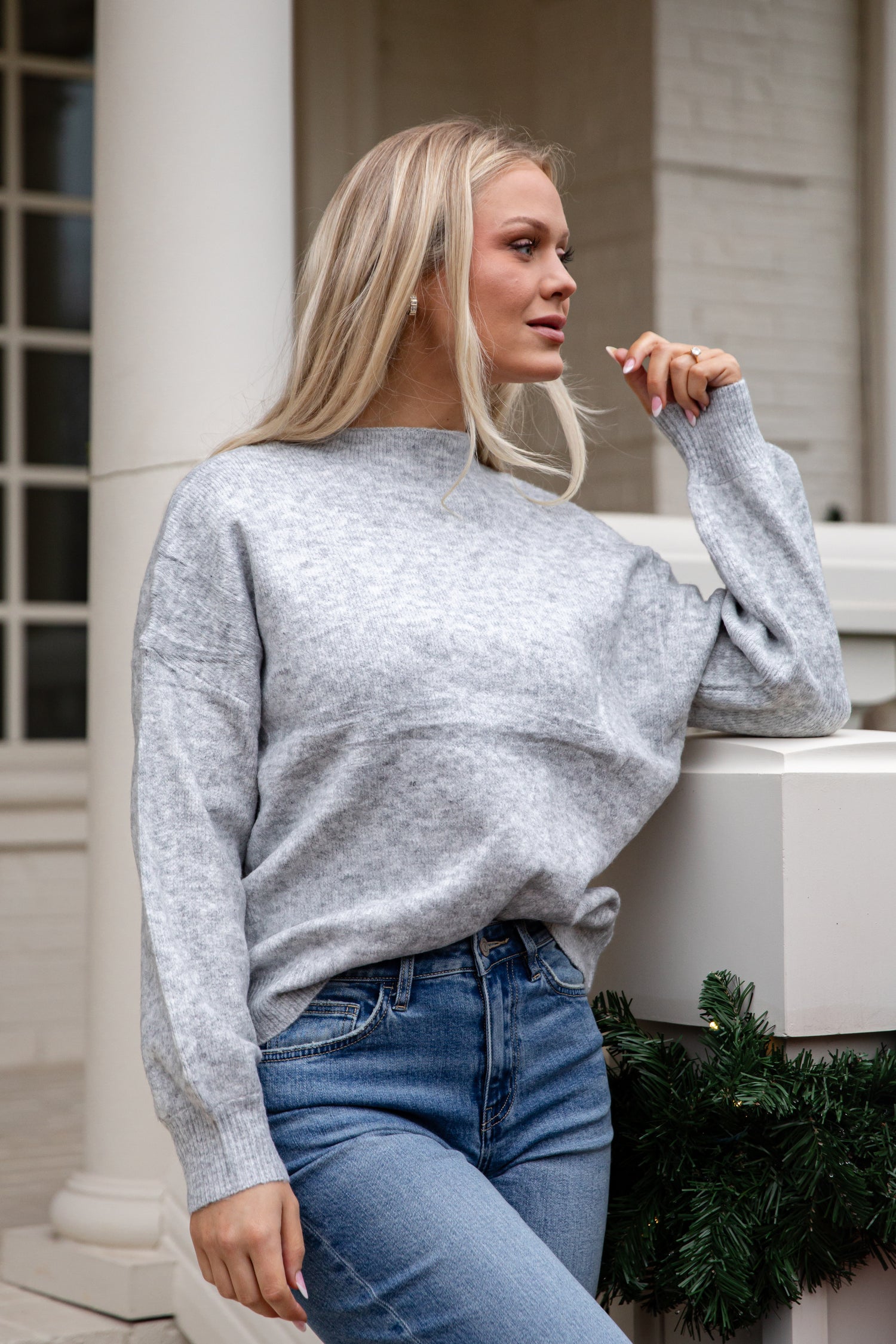 Woman wearing a gray sweater and blue jeans standing outdoors.