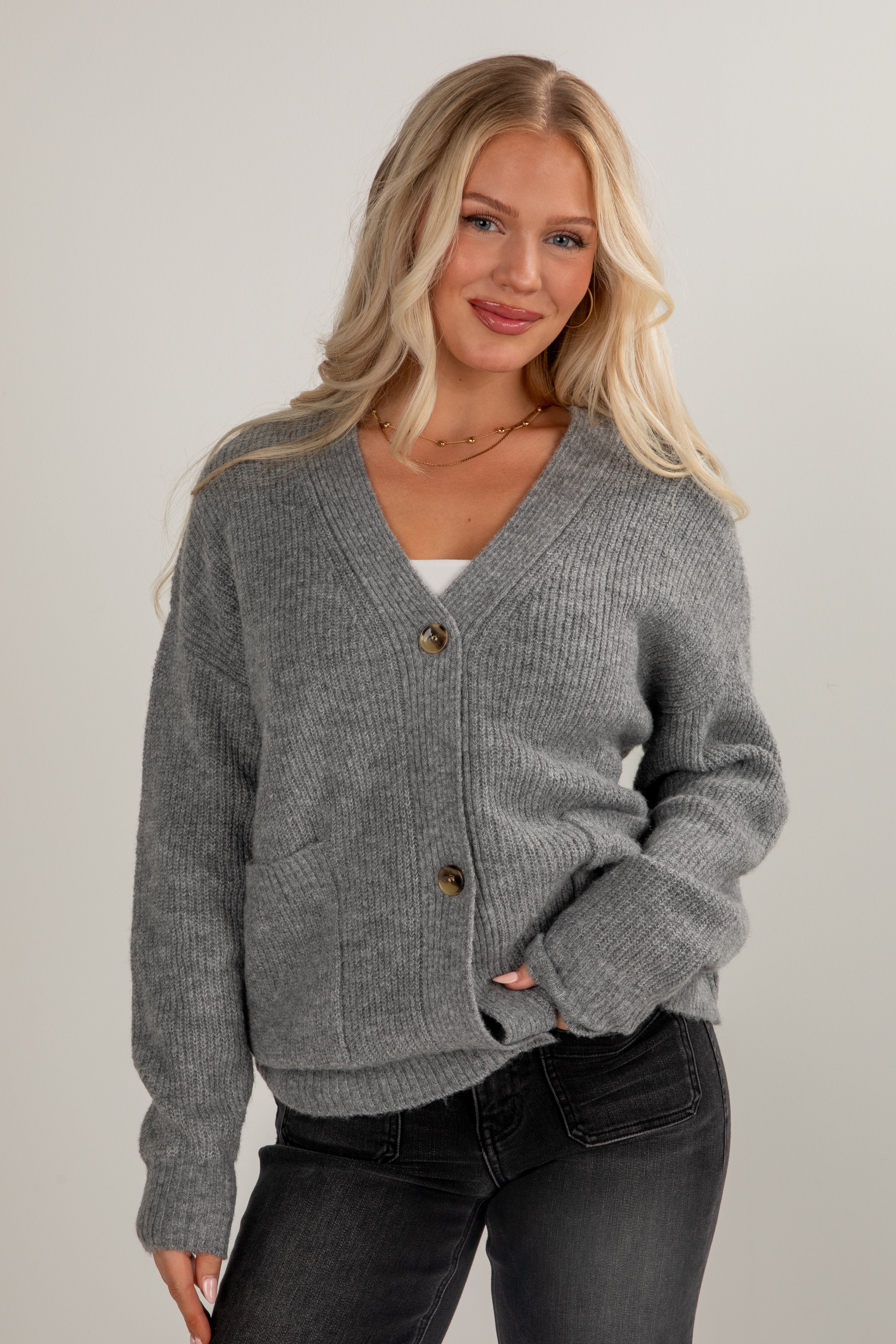 Woman wearing a gray cardigan with buttons on a plain background