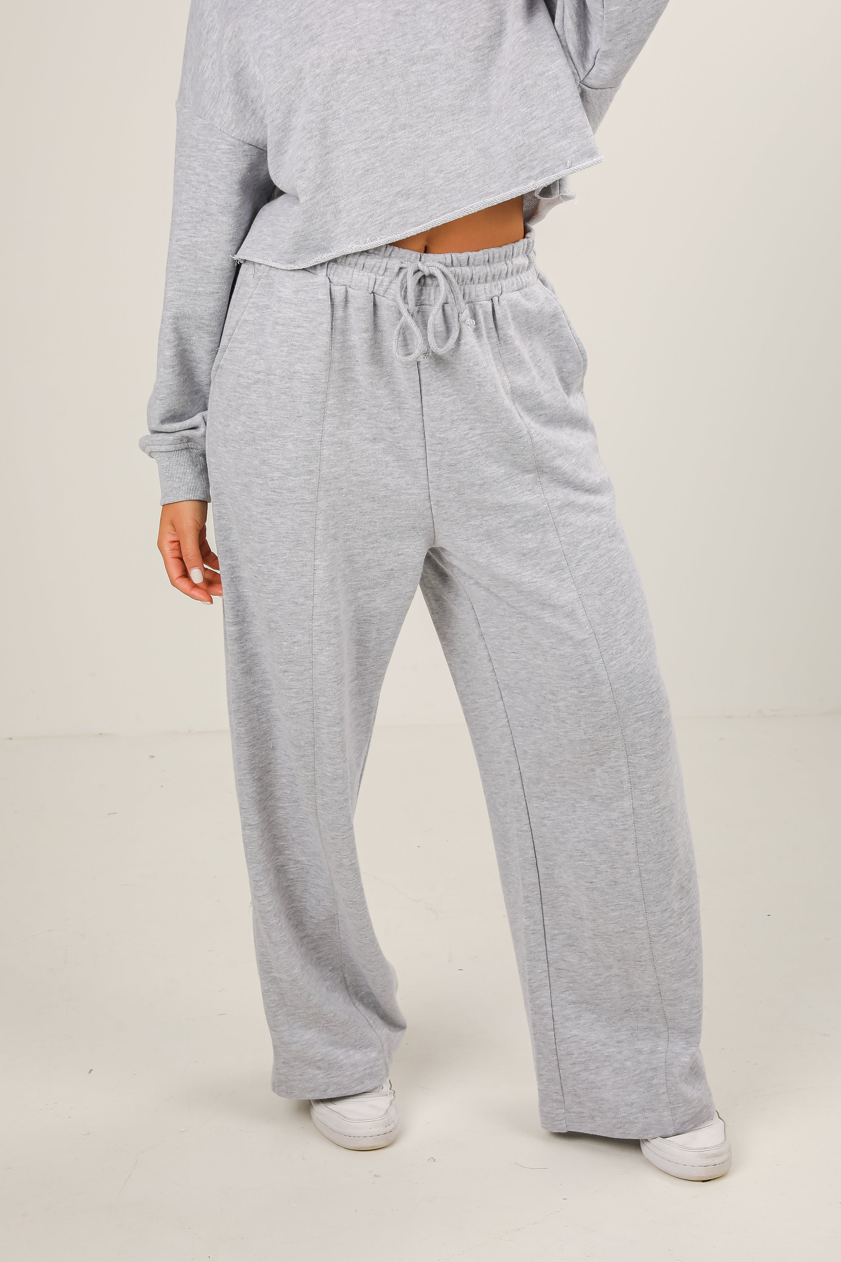 Person wearing gray sweatpants and a matching top on a plain background