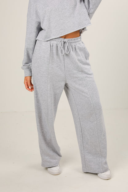 Person wearing gray sweatpants and a matching top on a plain background