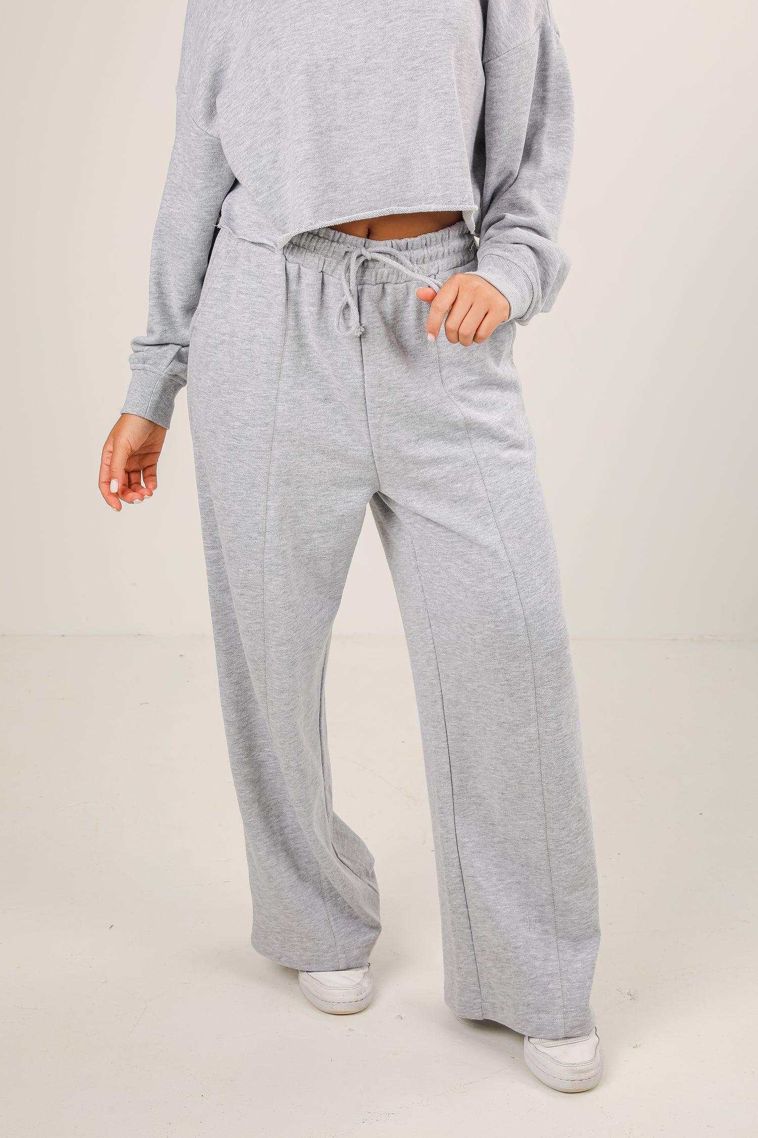 Person wearing gray sweatpants and a matching top on a plain background
