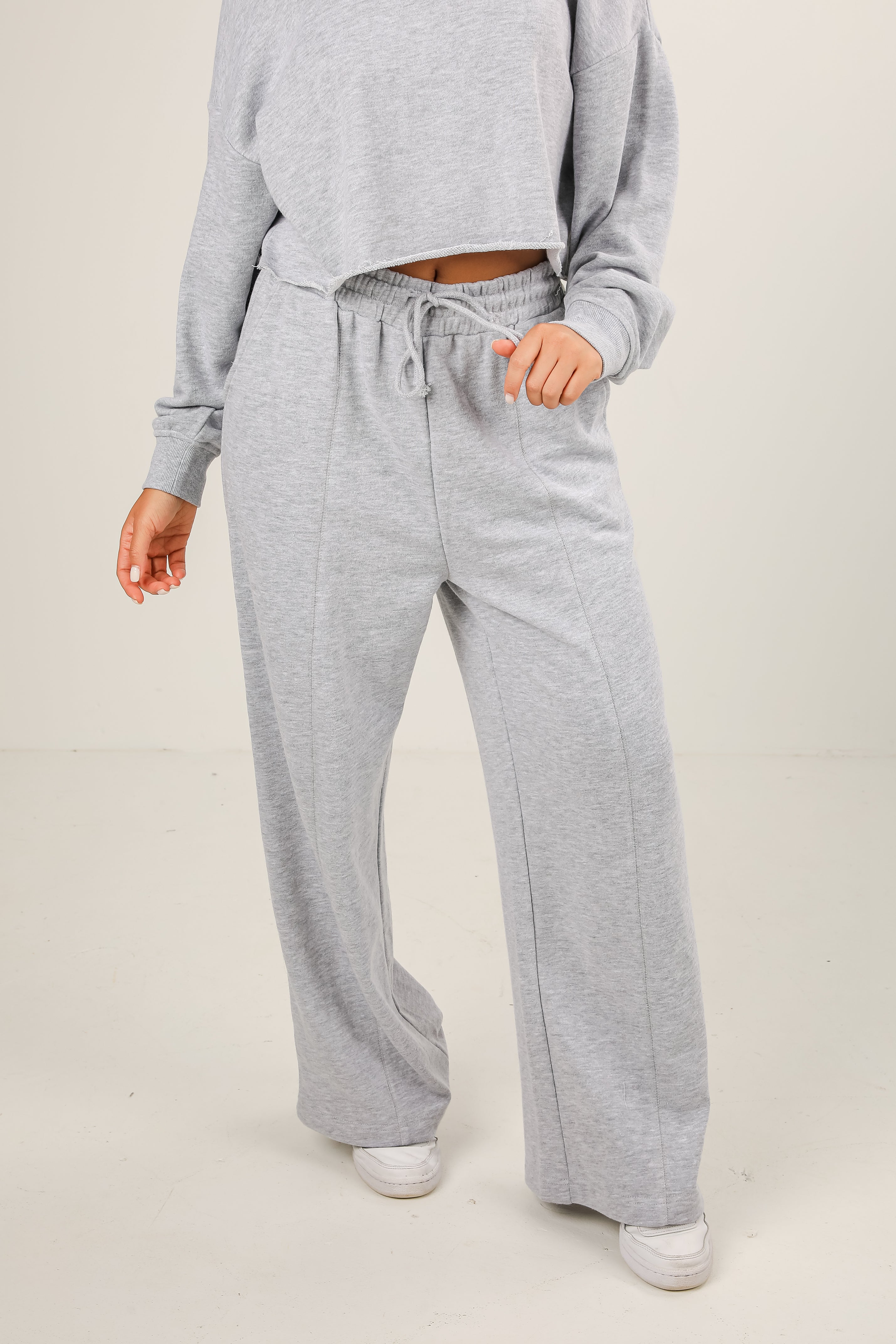 Person wearing gray sweatpants and a matching top on a plain background