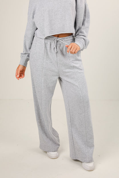 Person wearing gray sweatpants and a matching top on a plain background