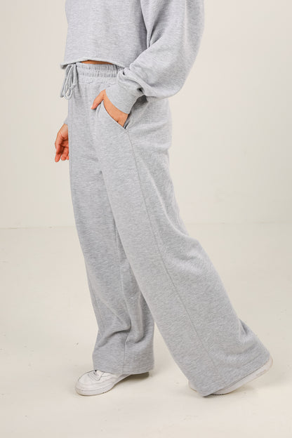 Person wearing gray sweatpants and a matching top on a plain background