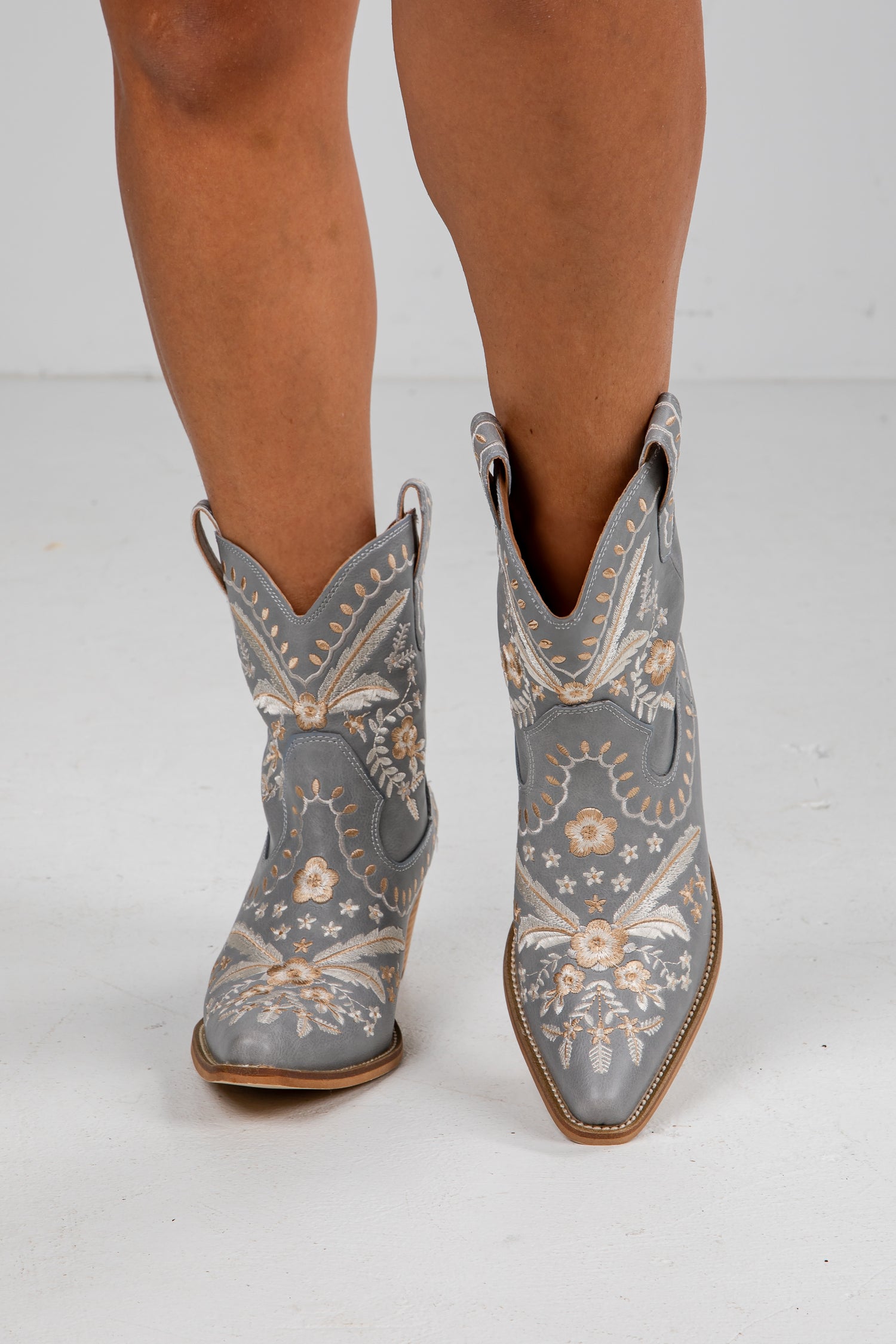 Gray cowboy boots with floral patterns worn by a person on a white background